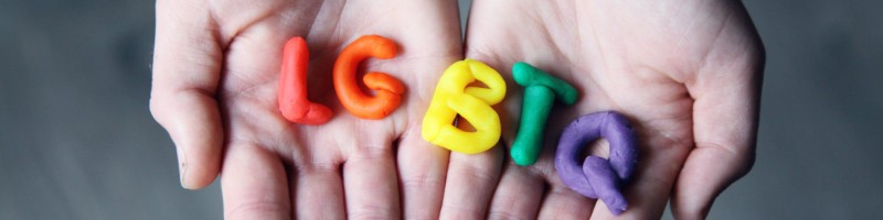 Hands holding clay moulds of the letters LGBTQ in rainbow colours