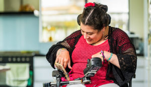 Woman in electric mobility aid. She is dressed in red and black with a red flower in her hair and using her phone which is attached to a display.